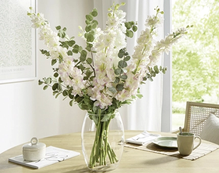 Heller Blumenstrauß aus zart rosafarbenen und weißen Blüten mit Eukalyptus in einer Glasvase auf einem Holztisch