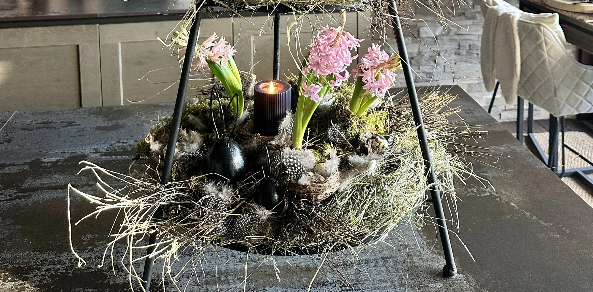 Osterdeko: Moosnest mit rosa Hyazinthen und schwarzen Deko‑Eiern in Metallständer