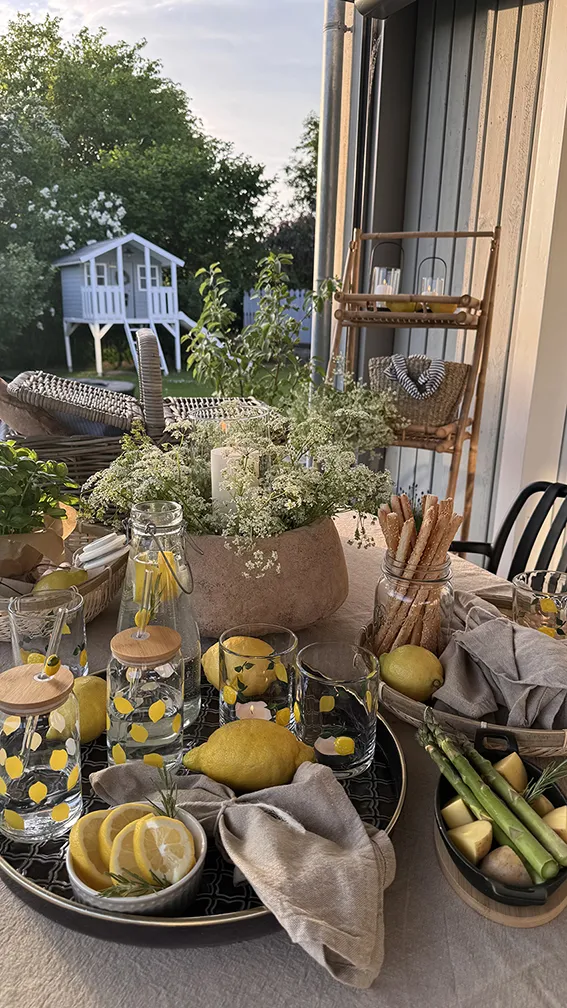 Tischdeko: sommerlich gedeckter Tisch mit Zitronen, Gläsern und Snacks im Garten